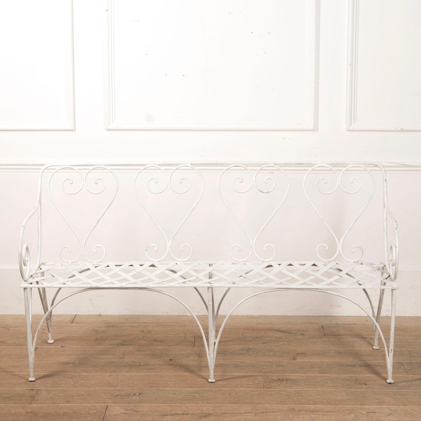 White metal bench with decorative backrest against a white wall.