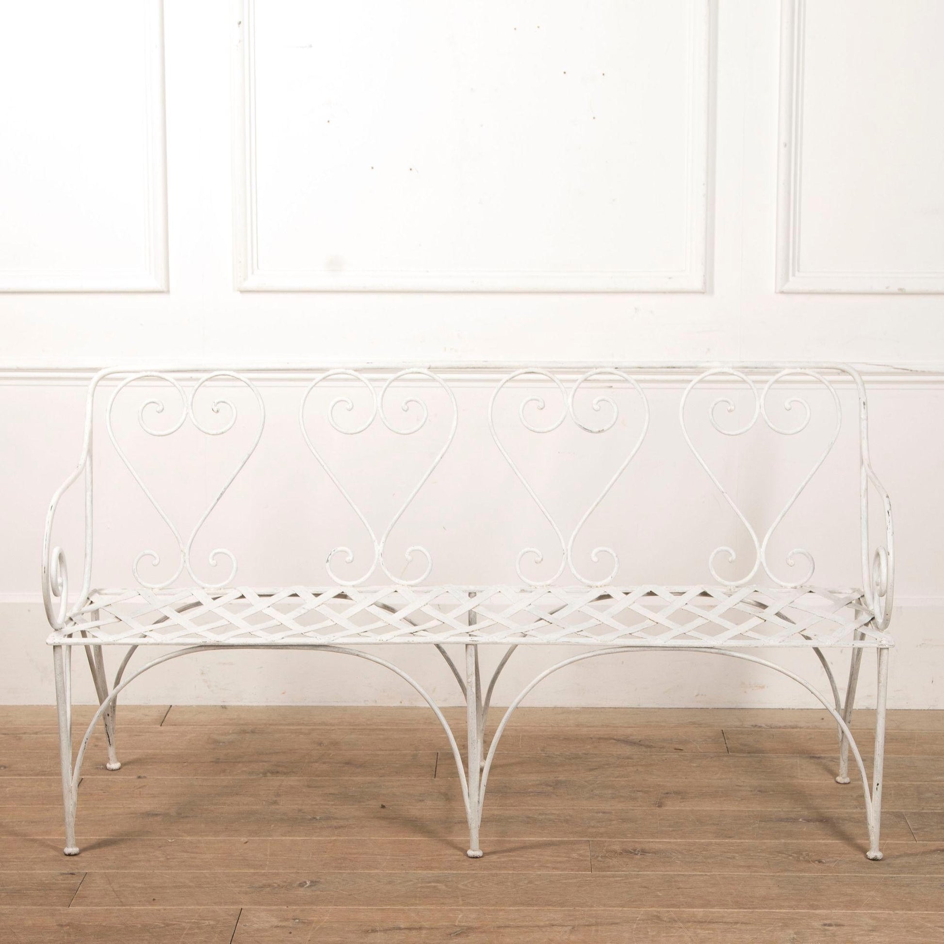 White metal bench with decorative backrest against a white wall.