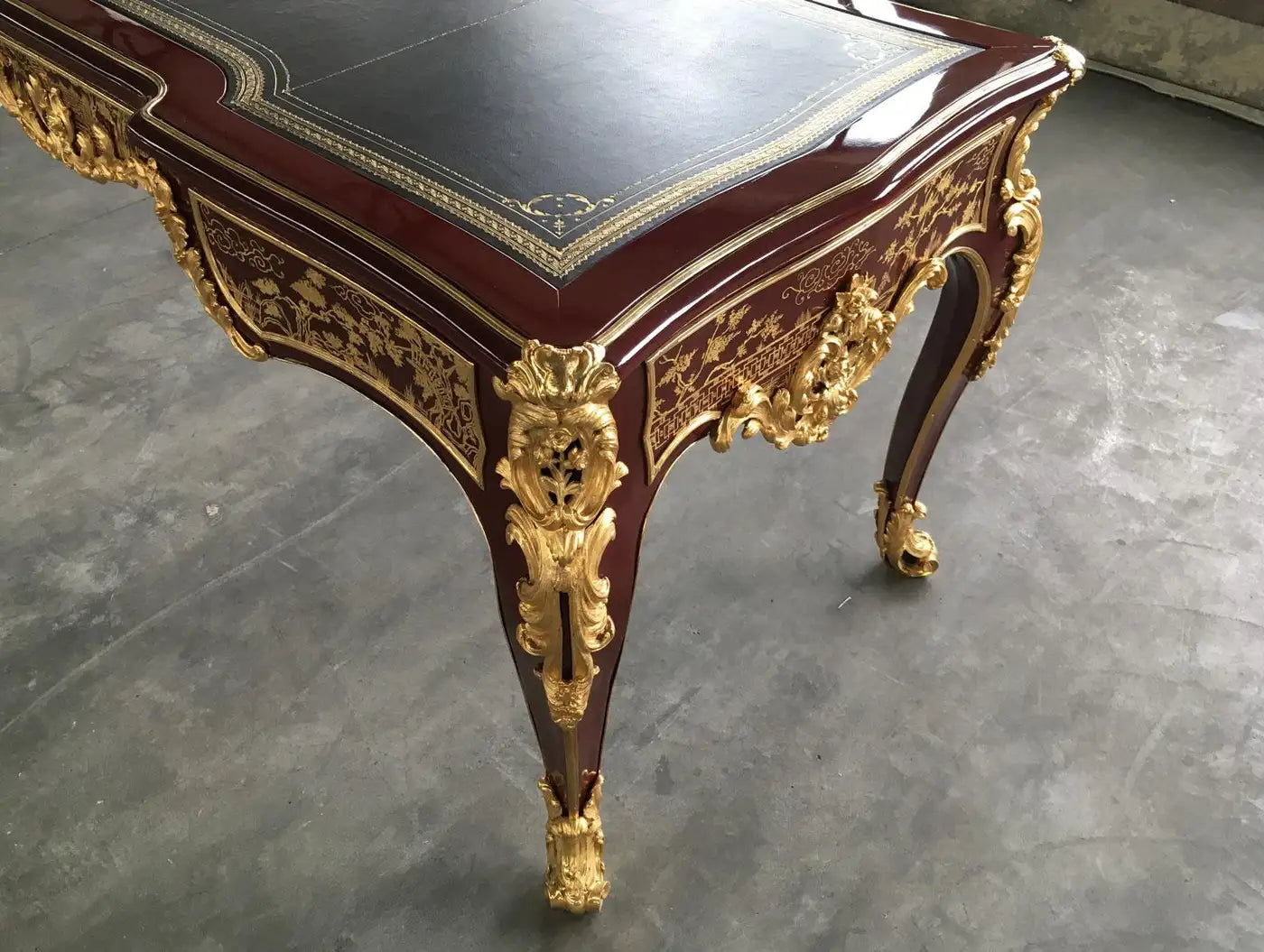 Decorative wooden table with gold embellishments on a gray floor.