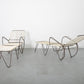 Two modern lounge chairs with metal frames and woven seats on a gray floor.