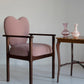Pink armchair with a wooden frame next to a small wooden table with two vases on a light gray background