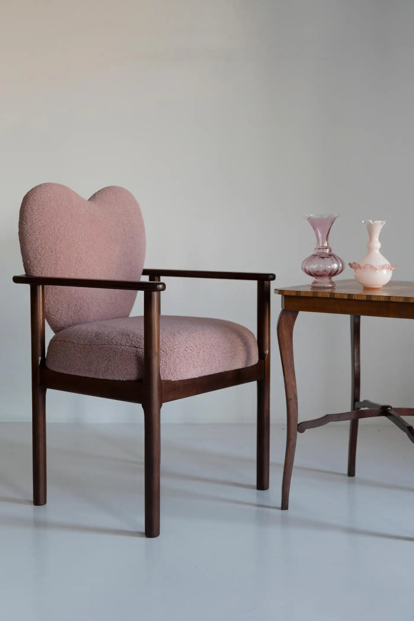 Pink armchair with a wooden frame next to a small wooden table with two vases on a light gray background