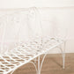 White metal bench with decorative backrest on a wooden floor.