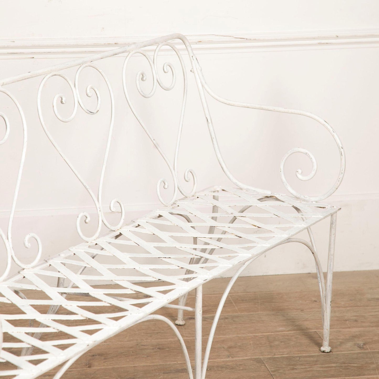 White metal bench with decorative backrest on a wooden floor.