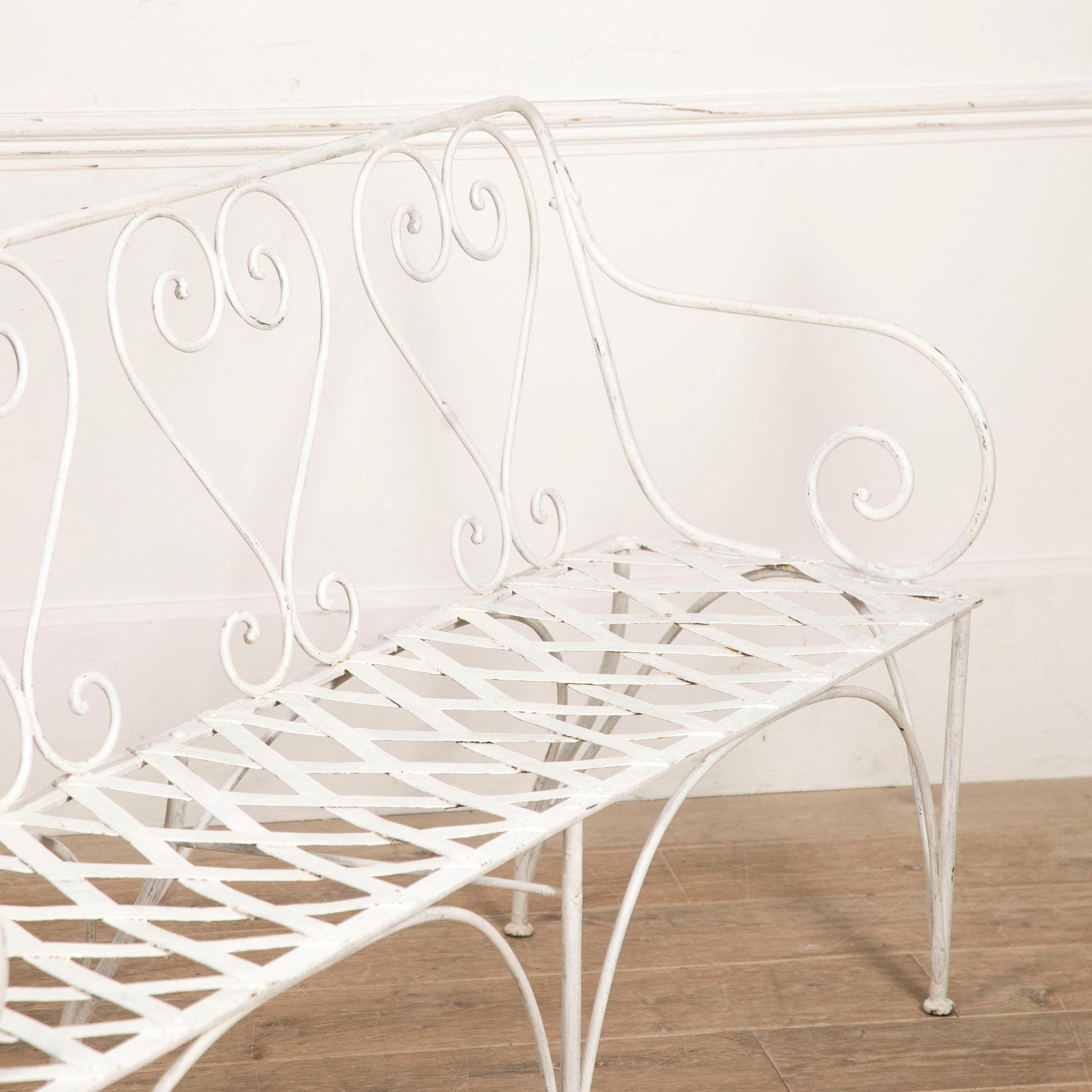 White metal bench with decorative backrest on a wooden floor.