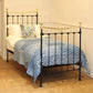 Bed with black metal frame, gold accents, and blue patterned bedding in a room.