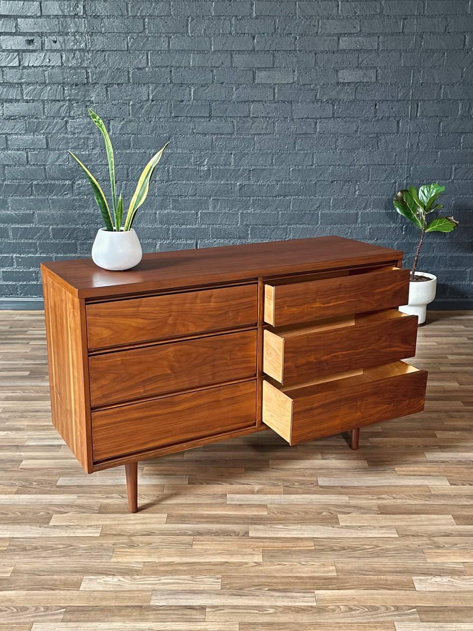 Wooden dresser with three drawers against a brick wall.