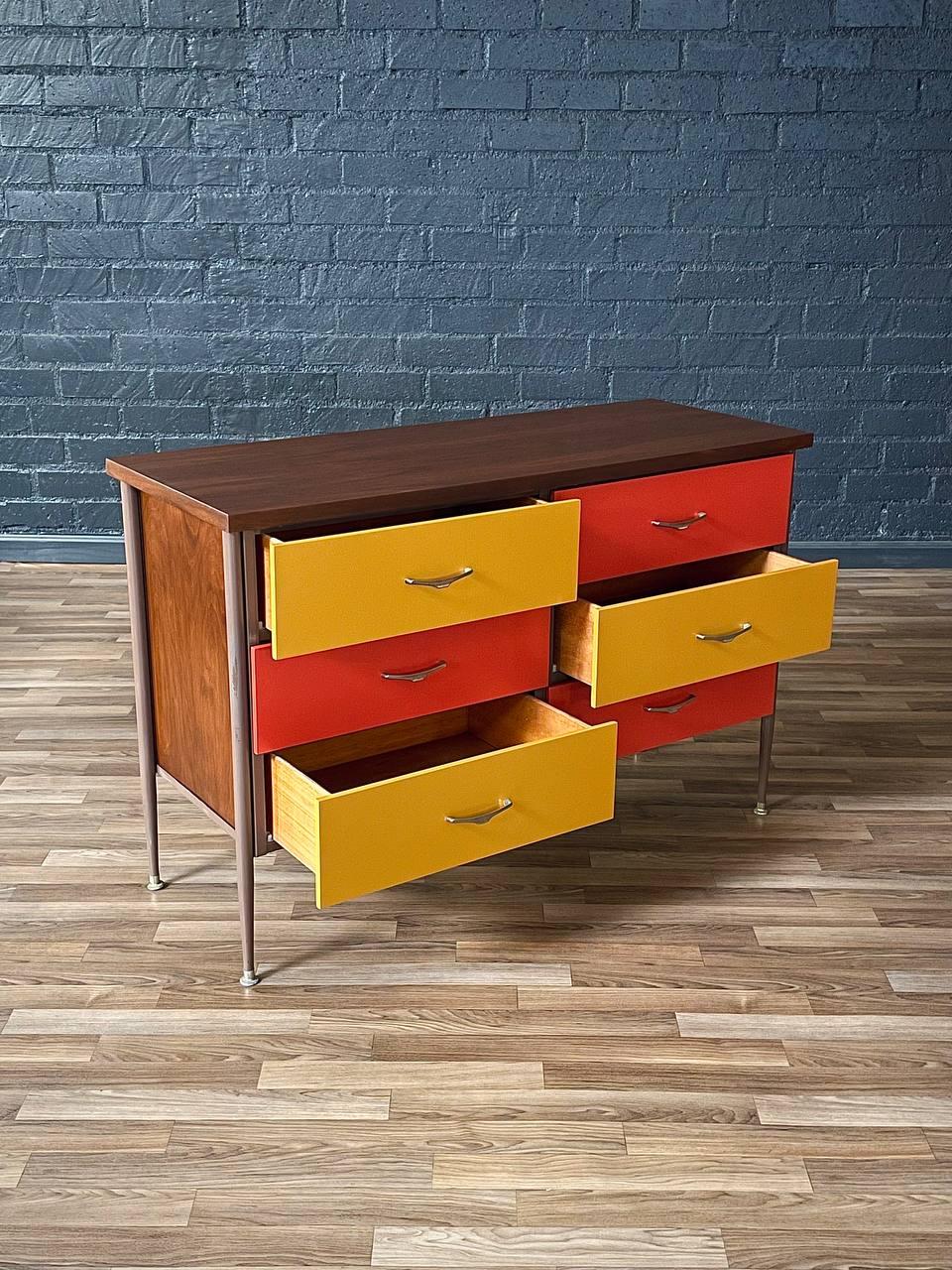 Multicolored dresser with yellow, red, and brown drawers against a blue brick wall.
