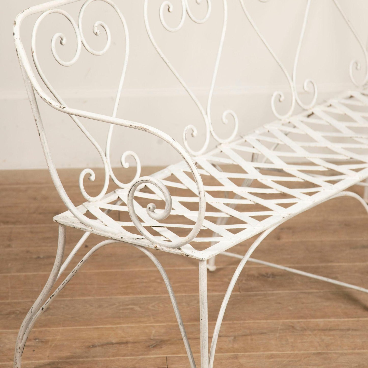 White metal bench with decorative scrollwork on a wooden floor.