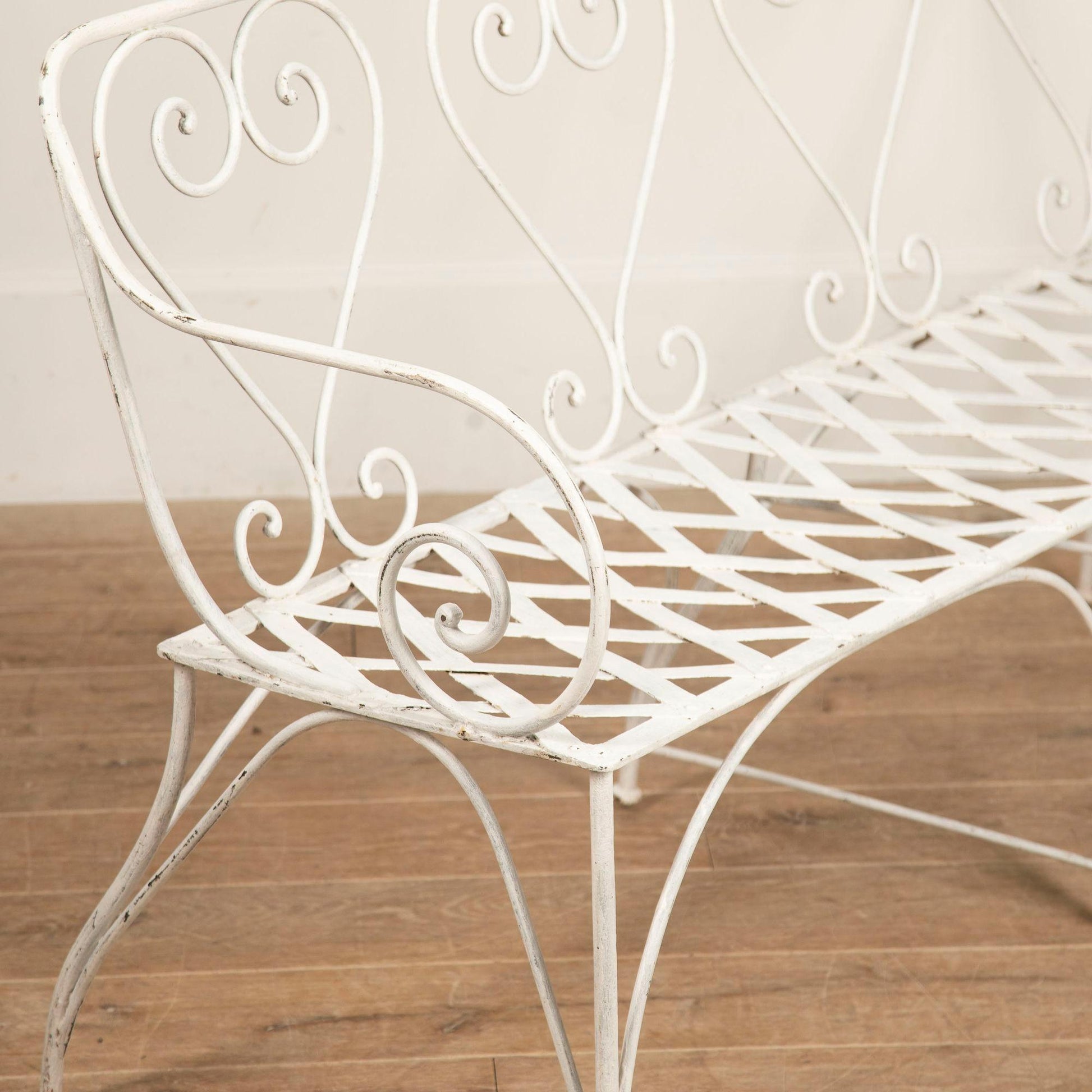 White metal bench with decorative scrollwork on a wooden floor.