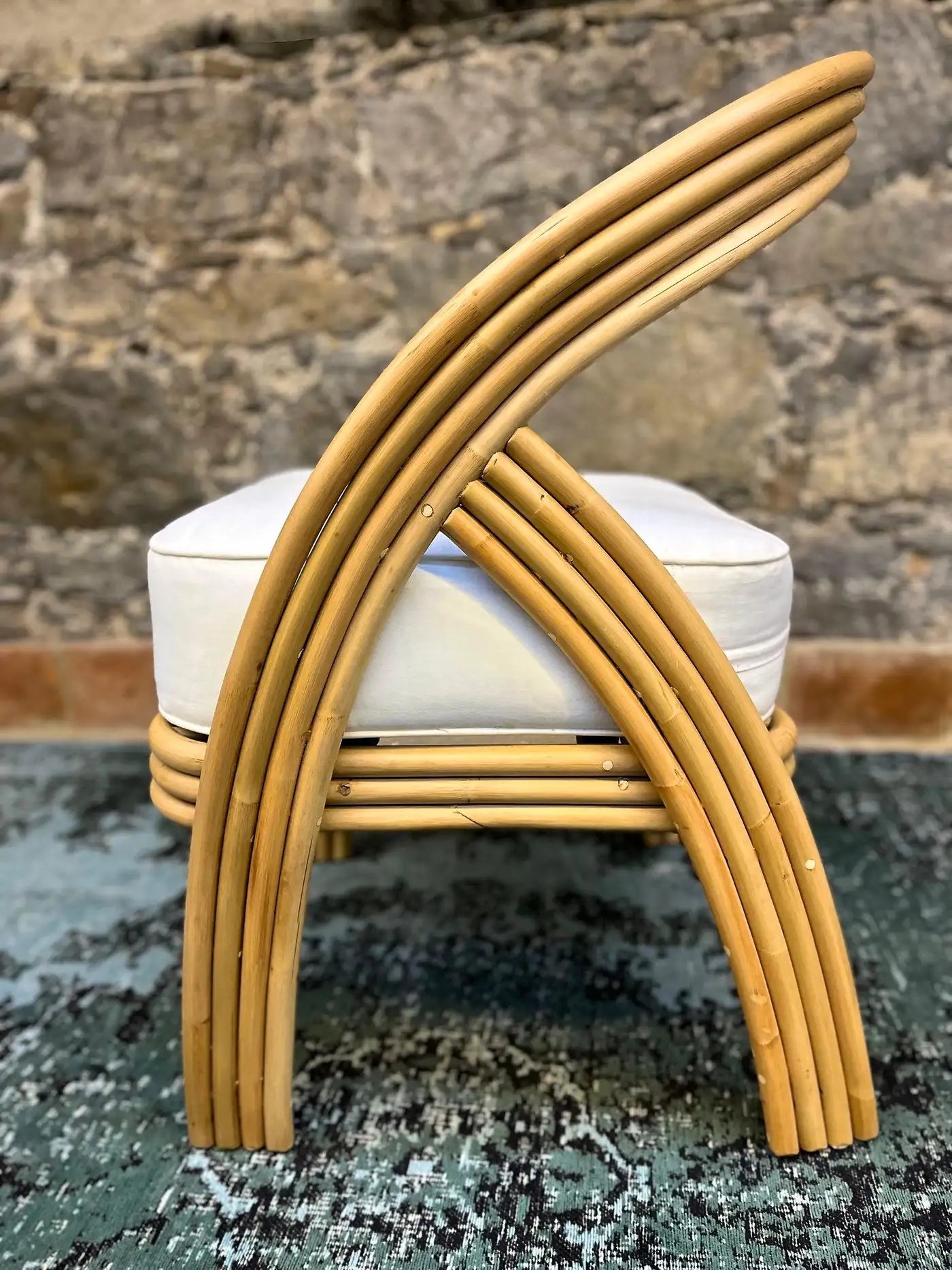 Rattan chair with a white cushion against a stone wall background