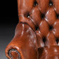 Close-up of a brown leather armchair with buttoned backrest on a dark background