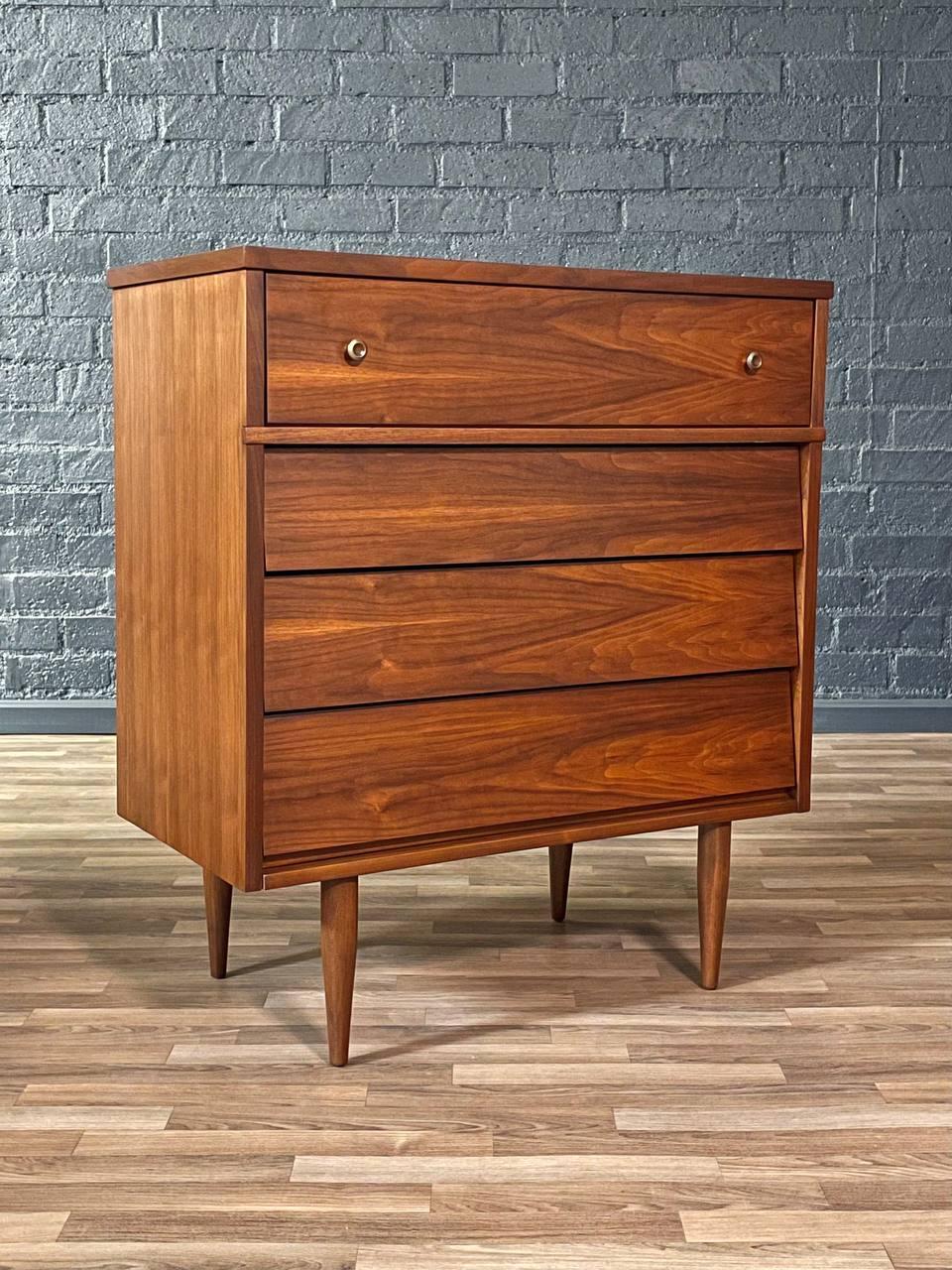 Wooden dresser with three drawers against a gray brick wall.