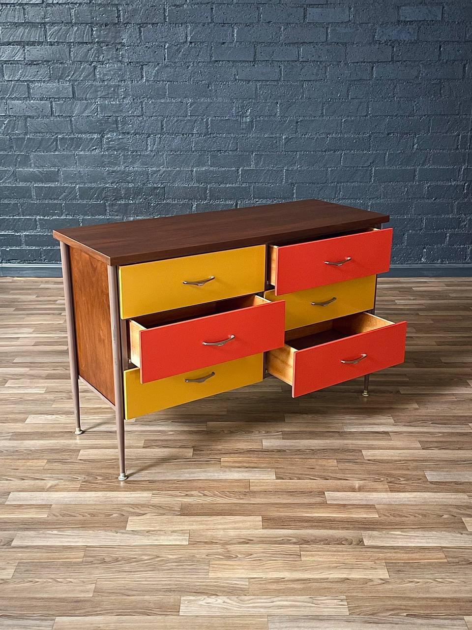 Colorful dresser with open drawers against a brick wall.