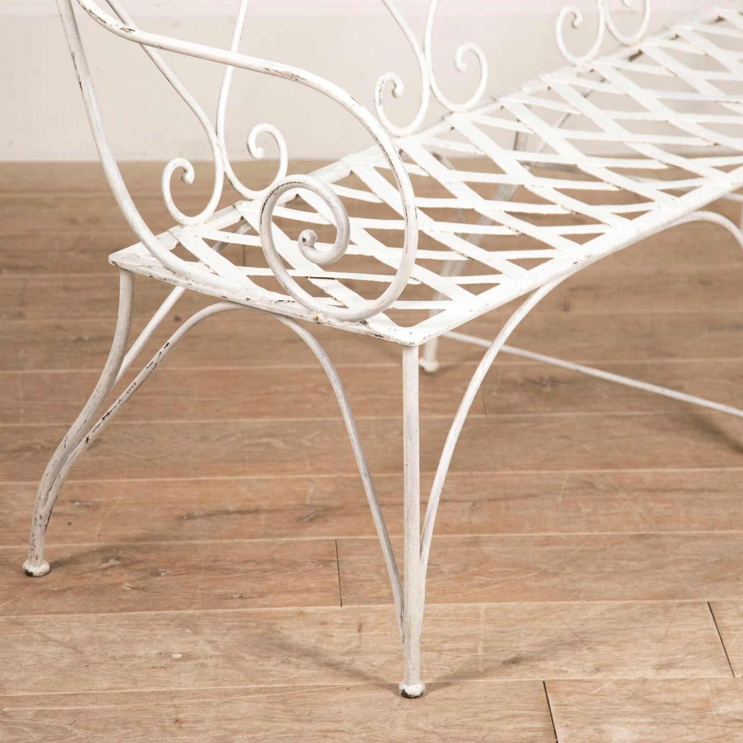 White metal bench with decorative armrests on a wooden floor