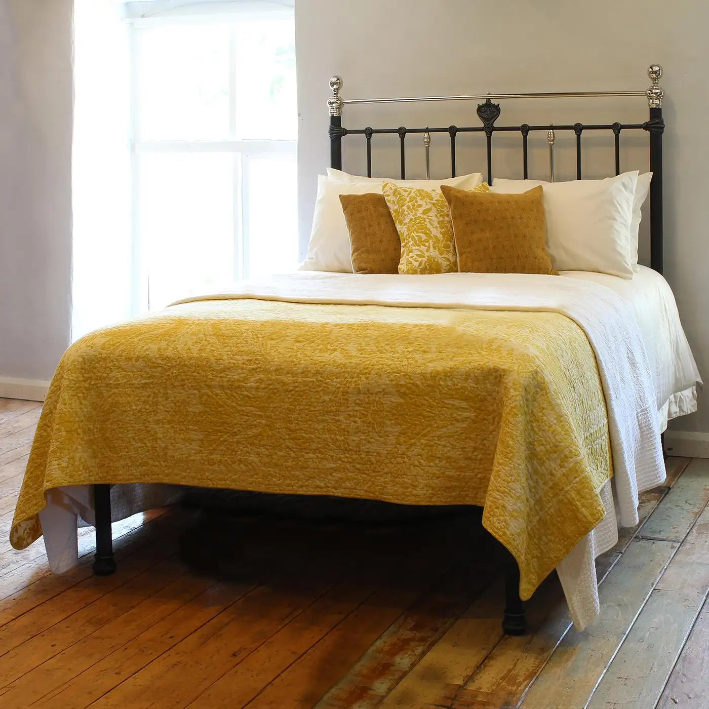 Bed with yellow blanket and pillows in a room with wooden floor and white walls