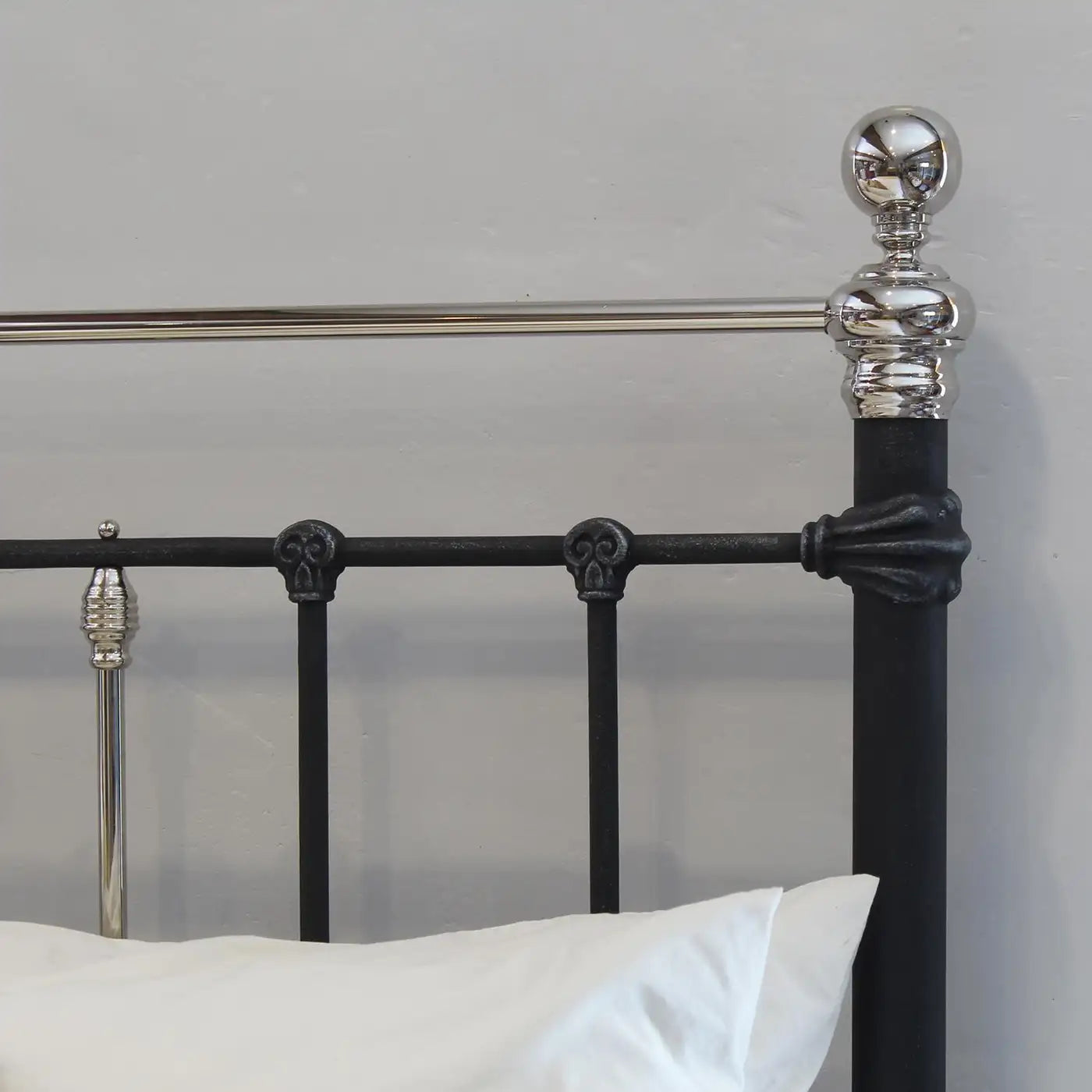 Close-up of a black metal bed frame with silver accents against a gray background.