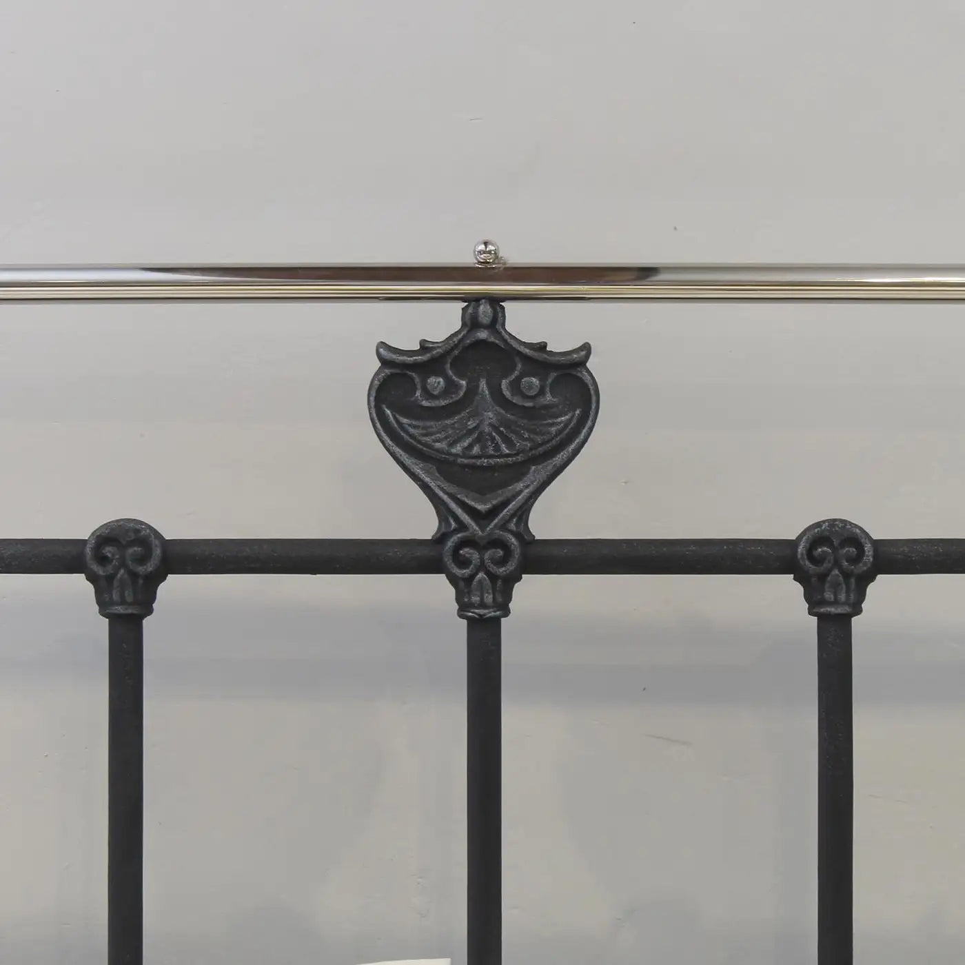 Decorative iron bed rail with intricate design on a plain background