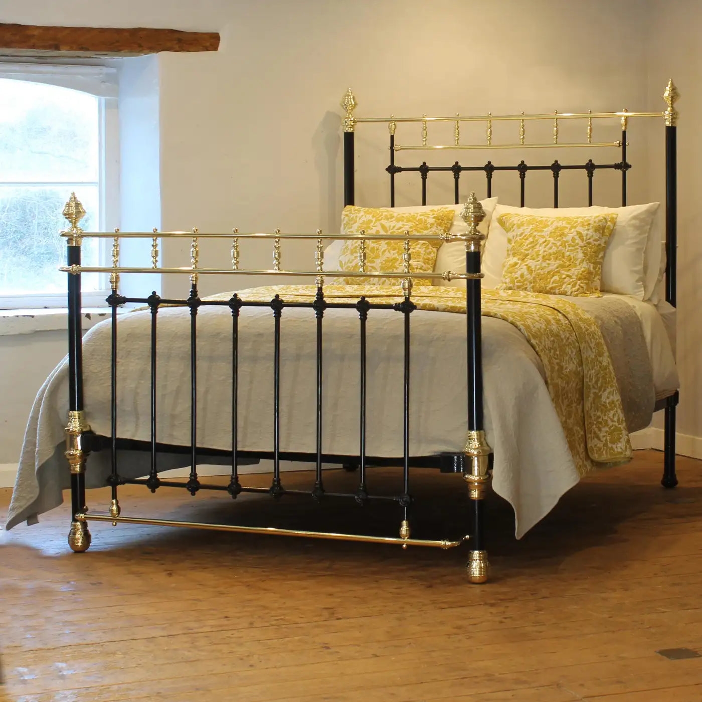 Bed with gold and black metal frame and yellow bedding in a room with a window.