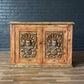 Wooden cabinet with decorative carvings against a dark brick wall.