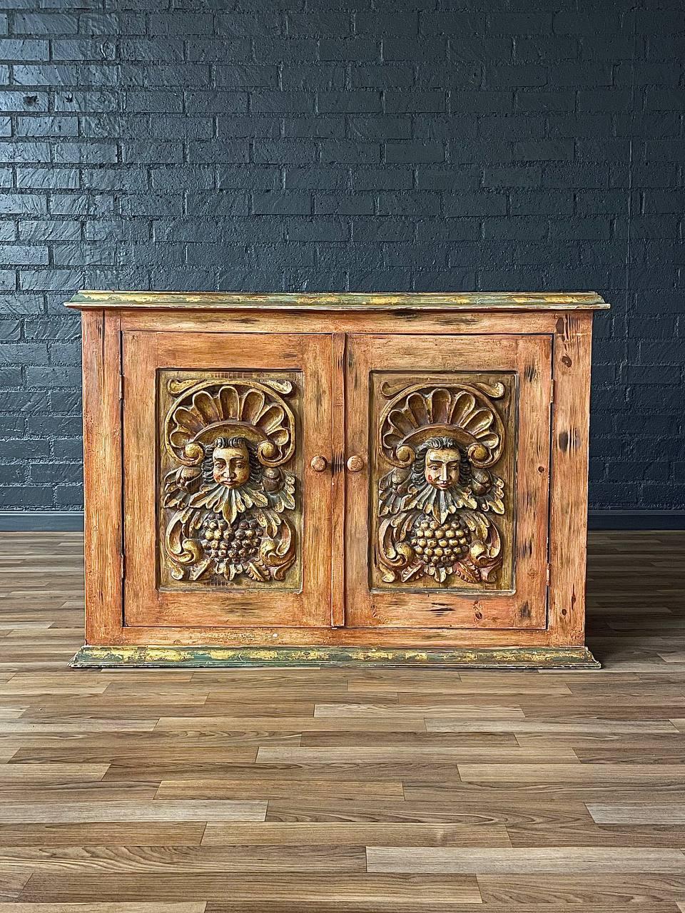 Wooden cabinet with decorative carvings against a dark brick wall.