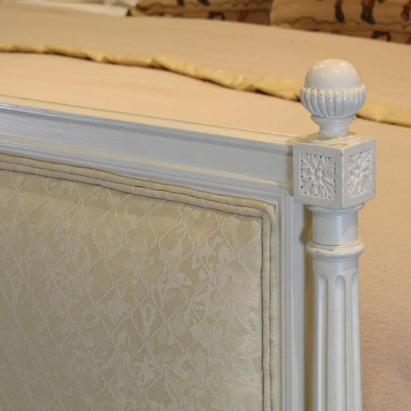 Close-up of a decorative bed frame with intricate carvings and a textured headboard.