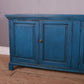 Blue wooden cabinet with two doors on a wooden floor against a gray wall.