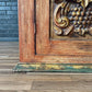 Wooden panel with intricate carvings on a wooden floor against a brick wall.