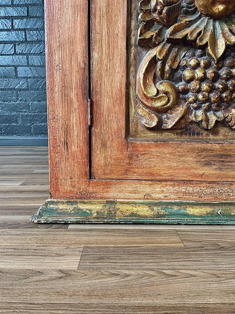 Wooden panel with intricate carvings on a wooden floor against a brick wall.