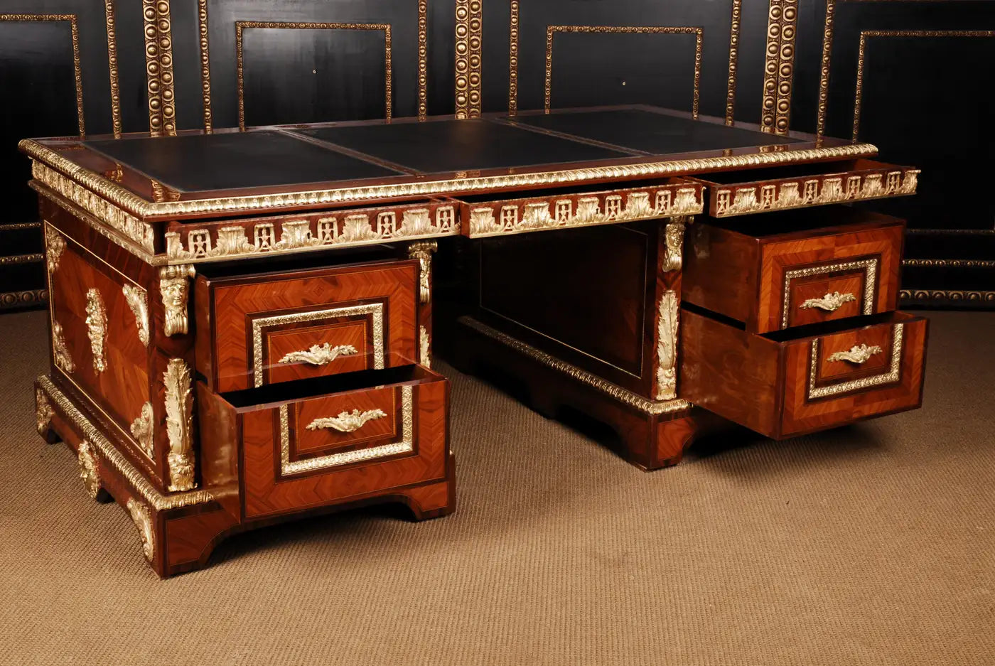 Vintage wooden desk with intricate carvings and gold accents against a dark patterned wall.