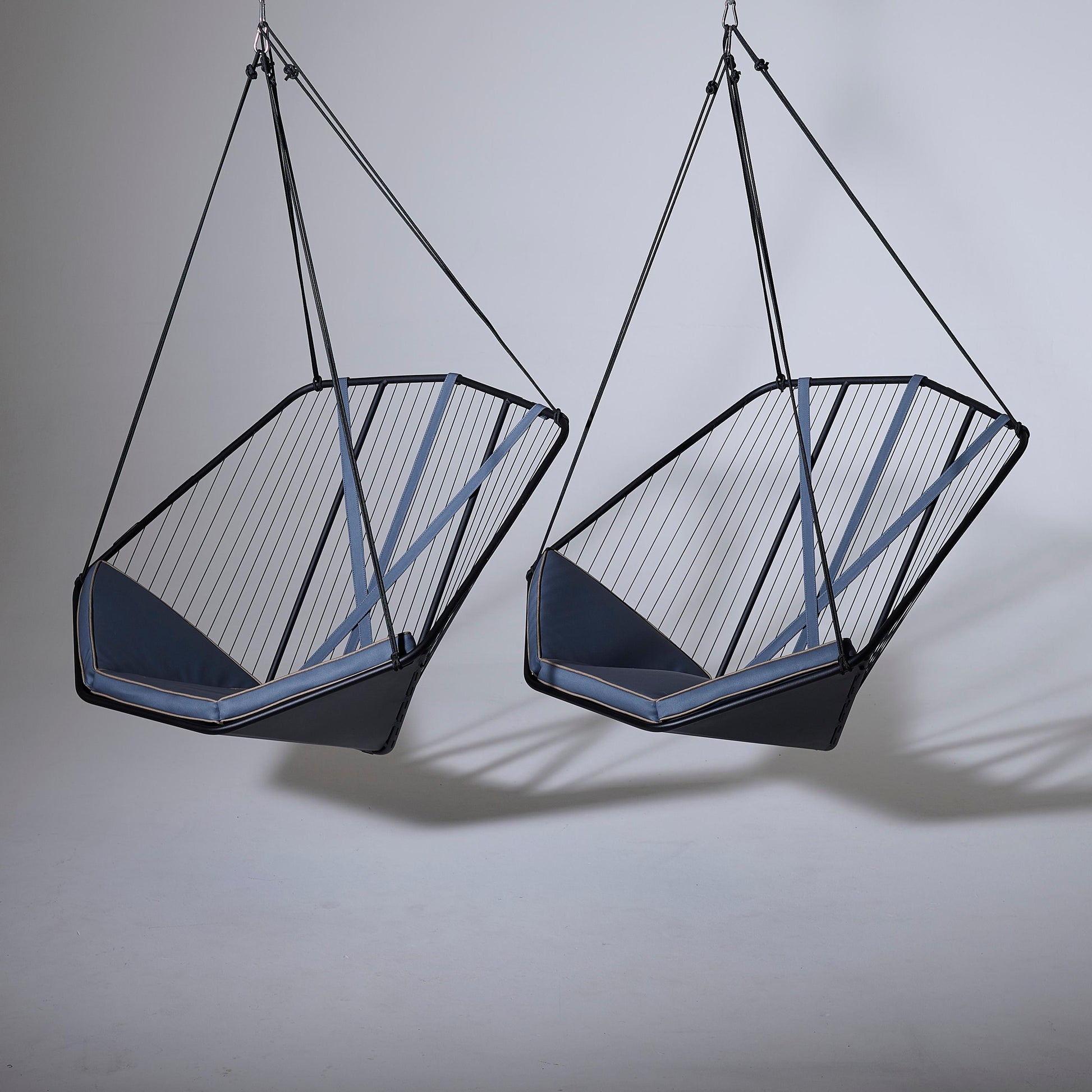 Two geometric hanging chairs with black frames and blue cushions on a gray background