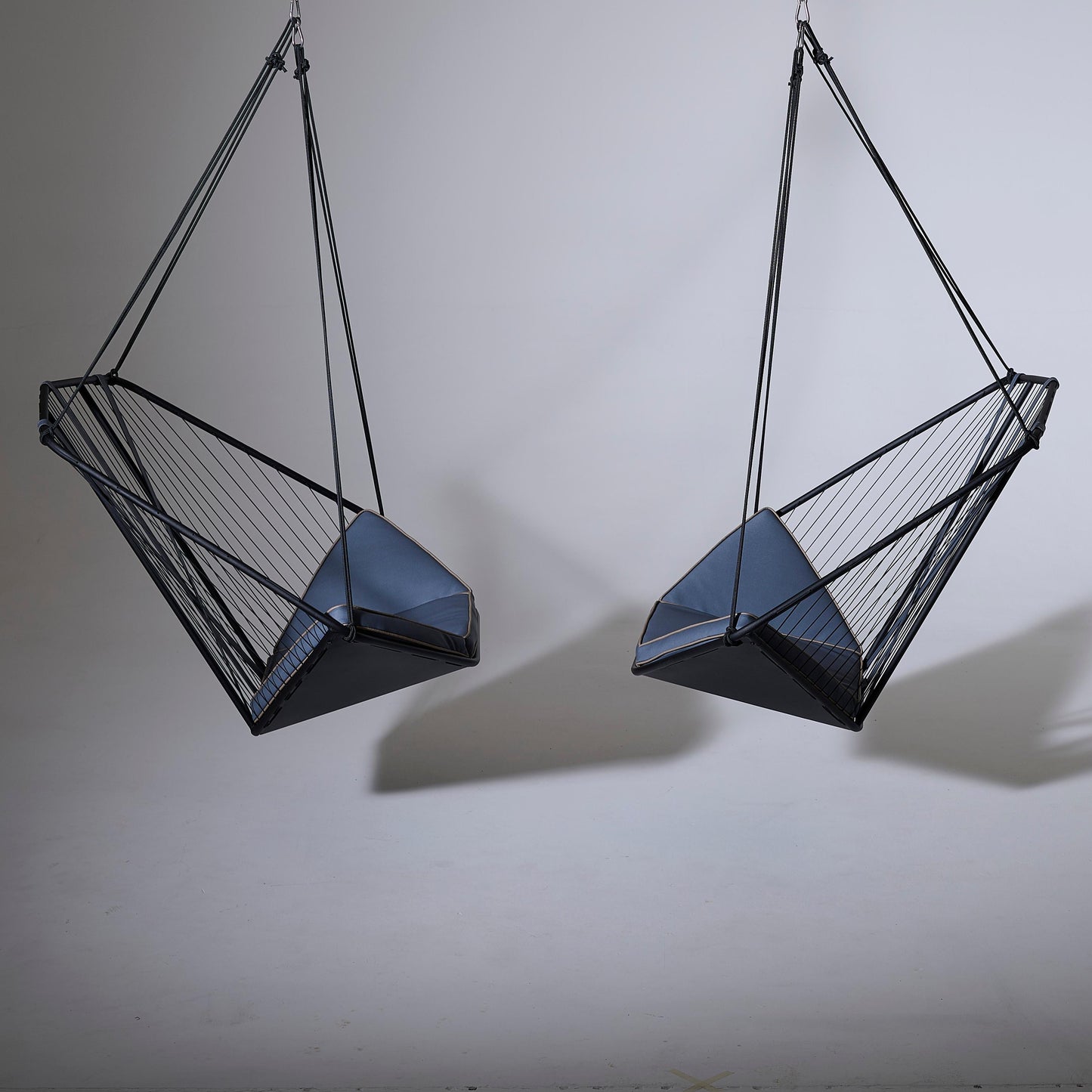 Two geometrically designed hanging chairs on a plain background