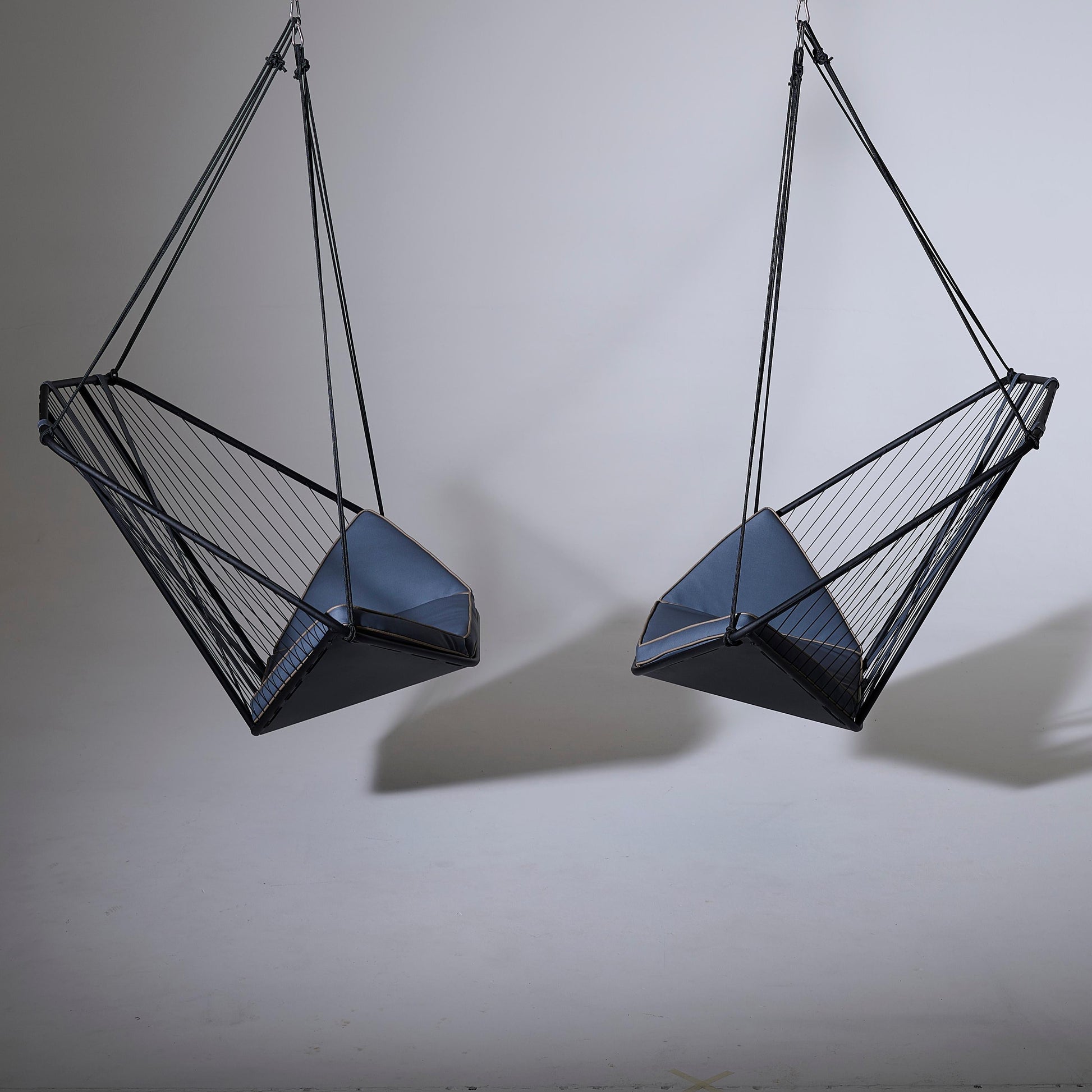 Two geometrically designed hanging chairs on a plain background