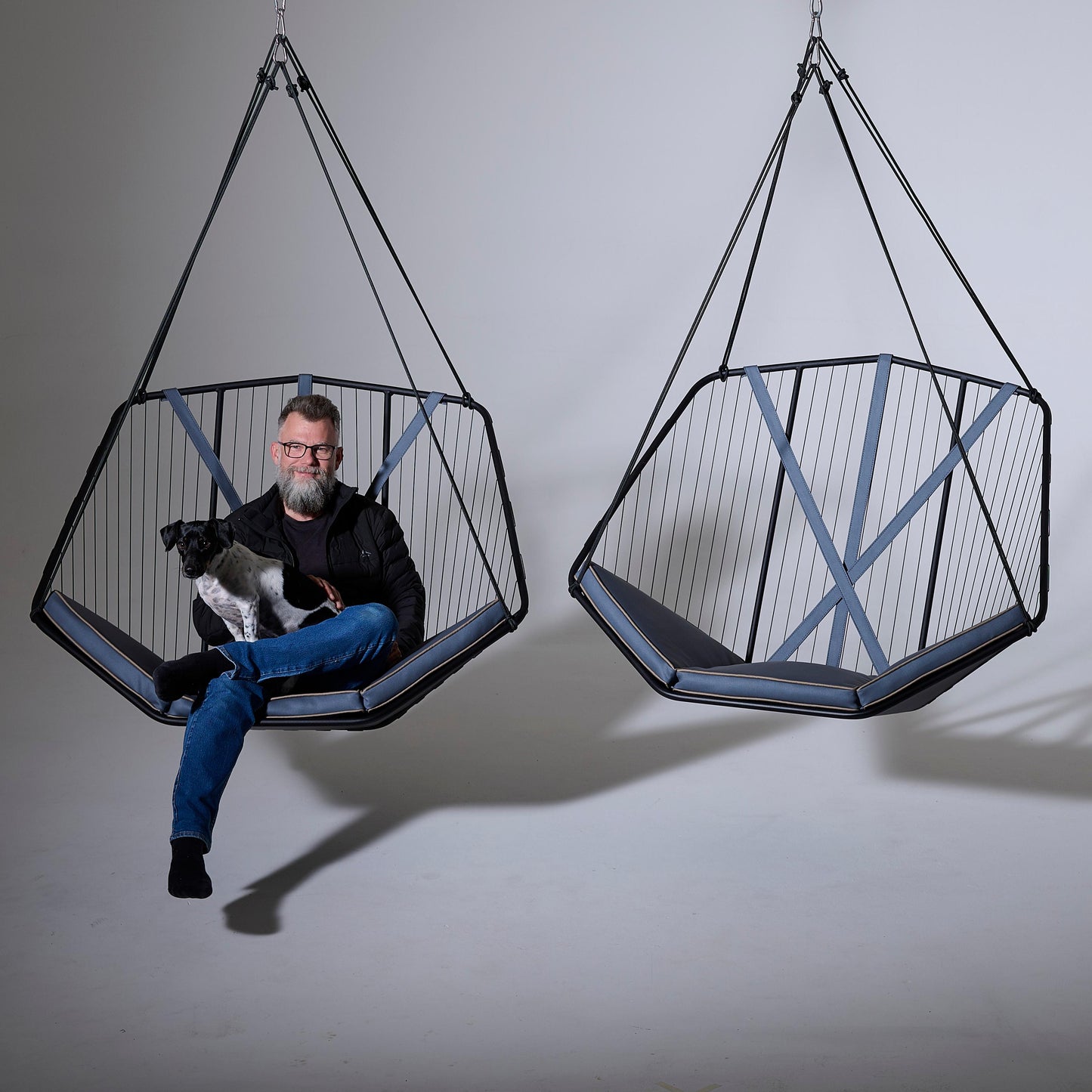 Person sitting in a geometric hanging chair with a dog, against a plain background