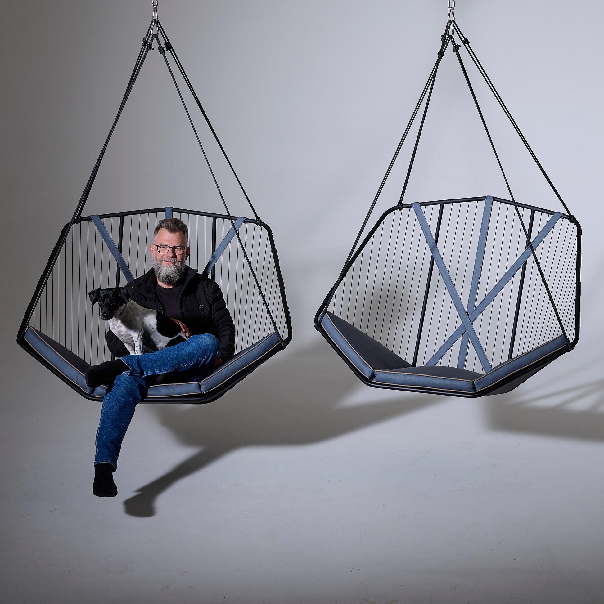 Person sitting in a geometric hanging chair with a dog, against a plain background