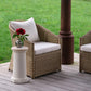 Wicker chair with white cushion and small table with red flowers on a wooden deck.