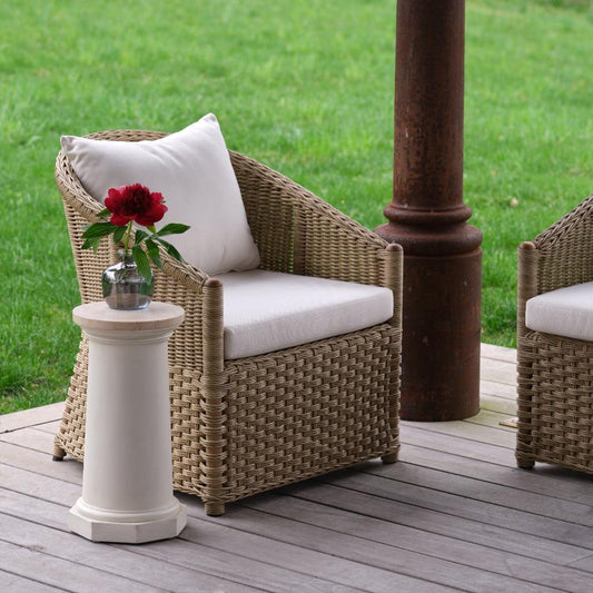 Wicker chair with white cushion and small table with red flowers on a wooden deck.