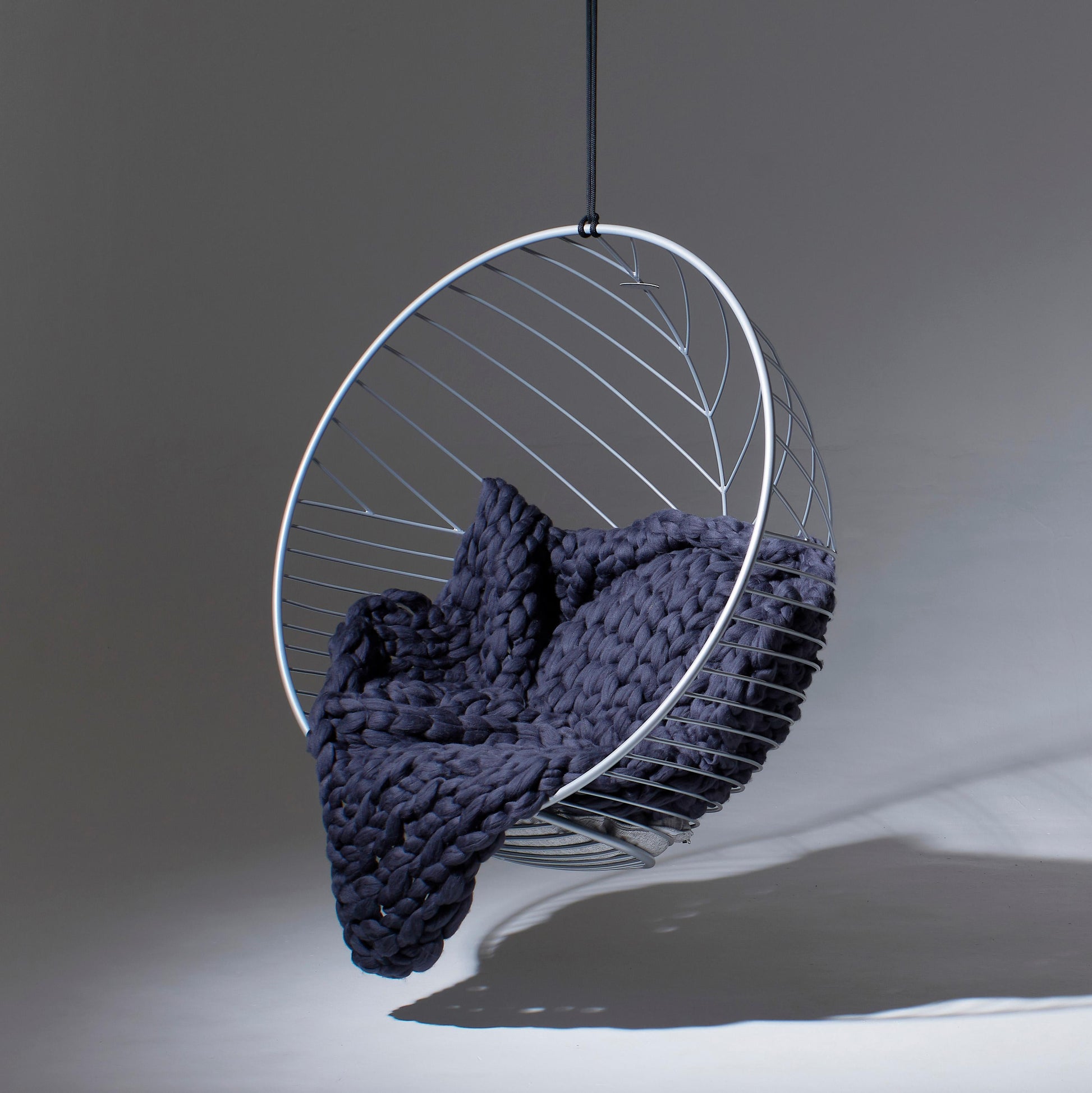 Modern hanging chair with a dark blue knitted blanket on a gray background