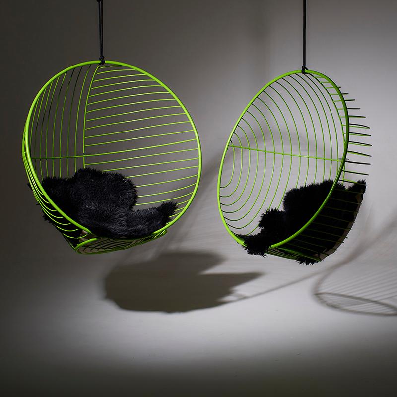 Two green wireframe hanging chairs with black cushions on a gray background