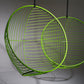 Two green wire mesh chairs hanging against a gray background