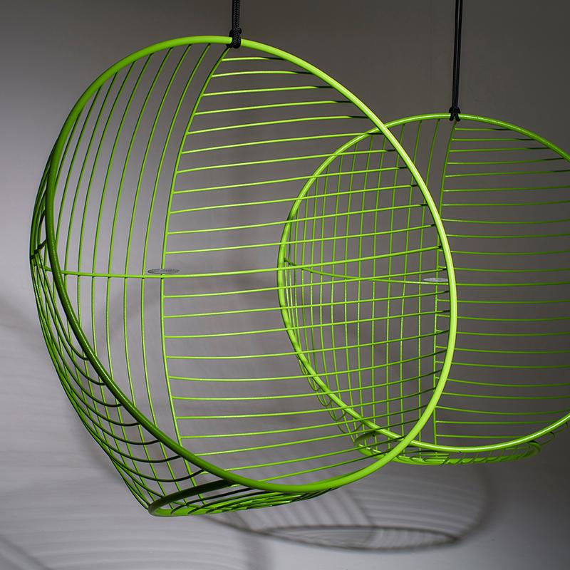Two green wire mesh chairs hanging against a gray background