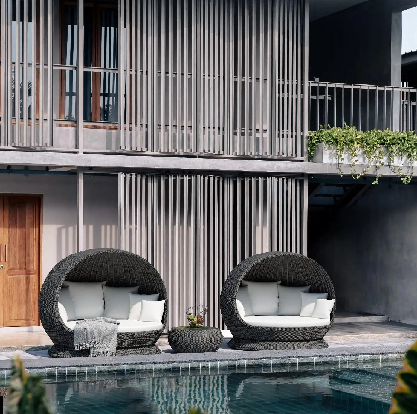 Two wicker chairs with cushions by a poolside in front of a modern building.