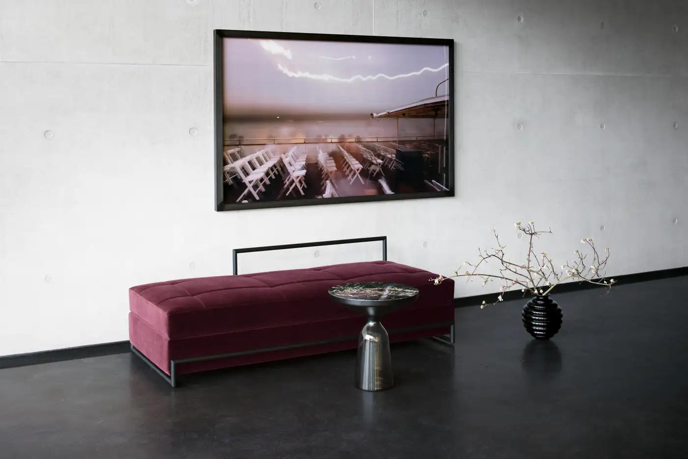 Modern interior with a pink bench, silver table, and decorative plant against a white wall.