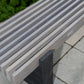 Gray bench on a paved surface with greenery in the background