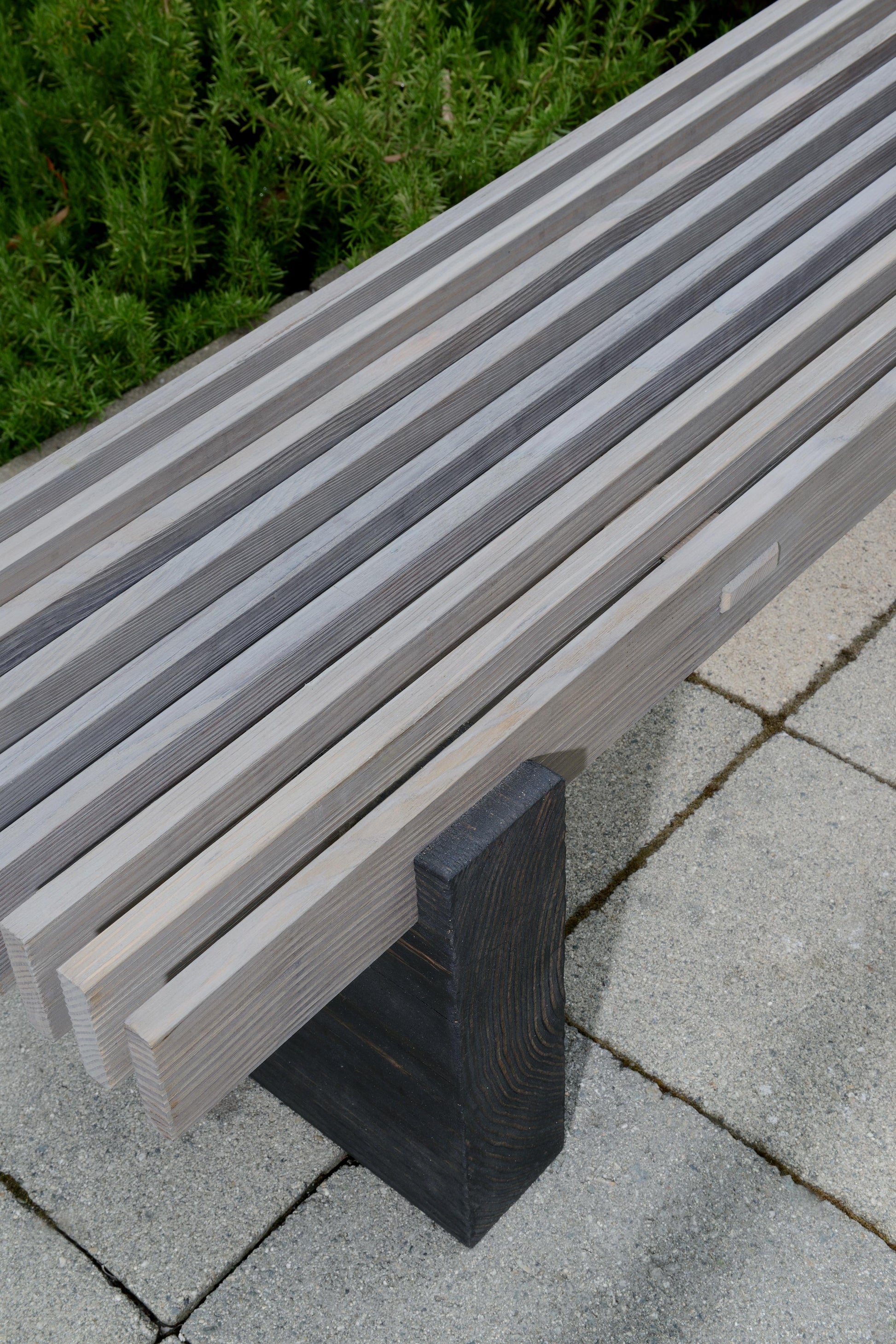 Gray bench on a paved surface with greenery in the background