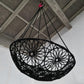 Black woven chair hanging from the ceiling against a white wall.
