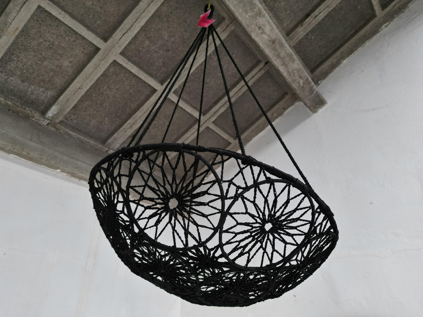 Black woven chair hanging from the ceiling against a white wall.