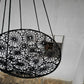 Black woven chair hanging from the ceiling against a white wall.