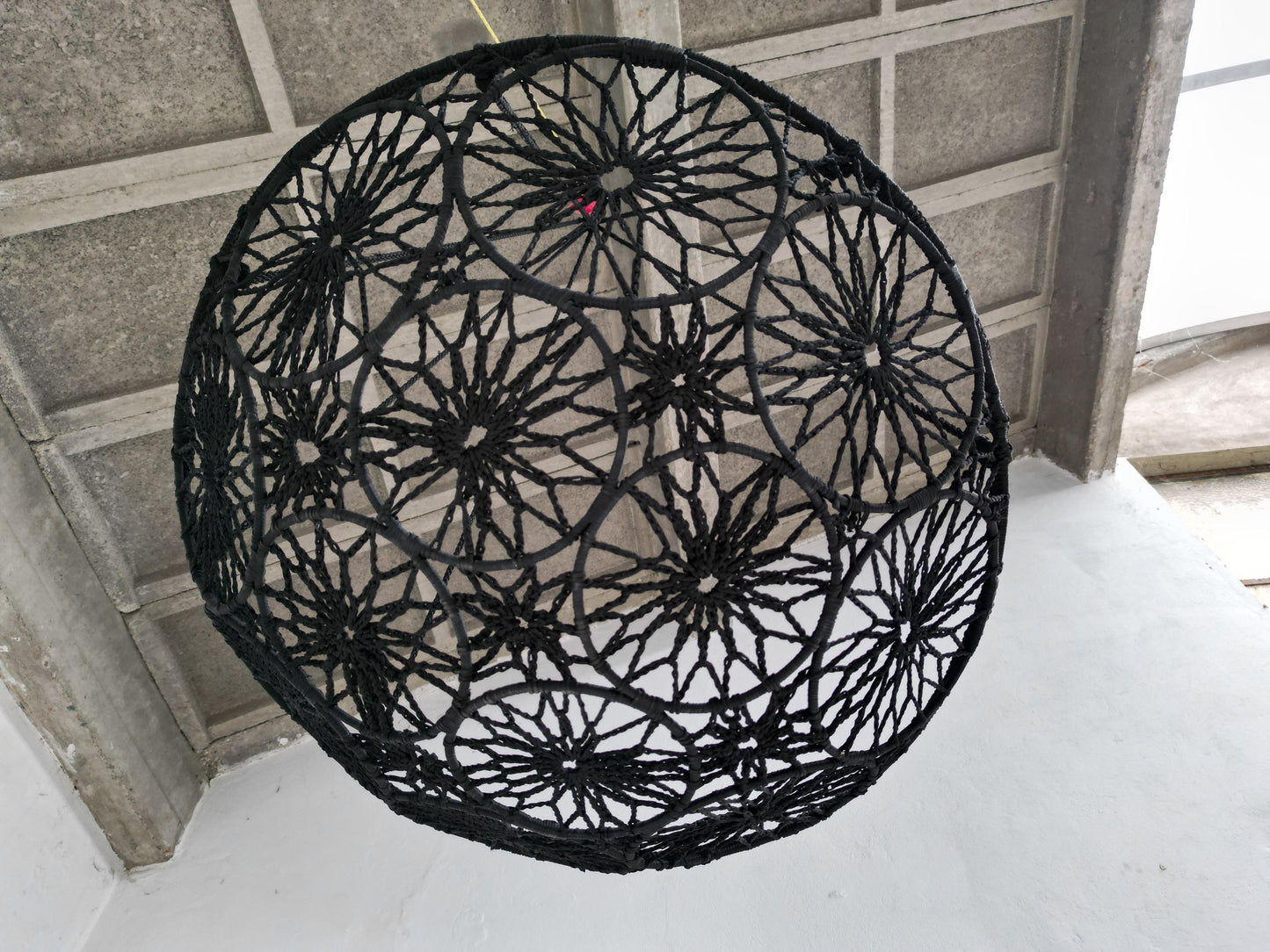 Black woven basket on a concrete floor with a tiled ceiling.