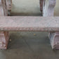 Pink stone bench with intricate carvings on a concrete floor